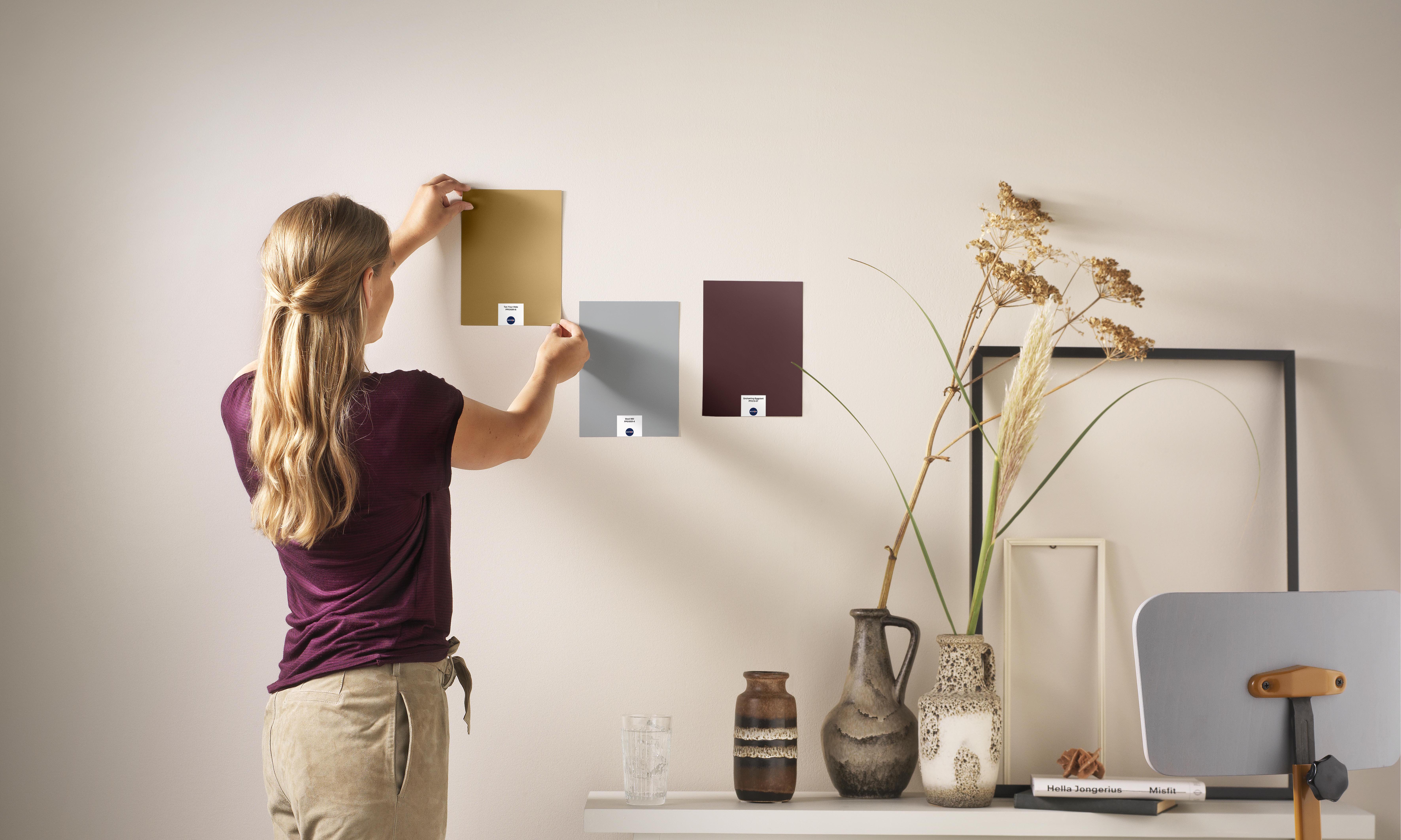 Een vrouw probeert 3 verschillende kleuren op een muur uit om te zien welke het beste past.